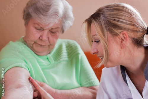 Altenpflegerin cremt Seniorin den Arm photo