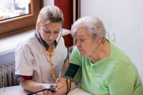 Altenpflegerin misst Blutdruck bei Patientin photo