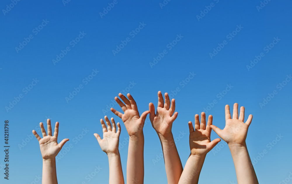 Many children hands raised up against blue sky with copy space