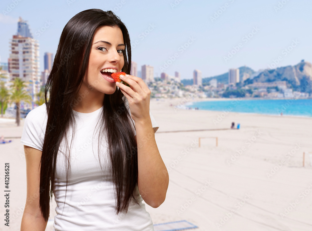 Fototapeta premium portrait of young woman eating strawberry against a beach