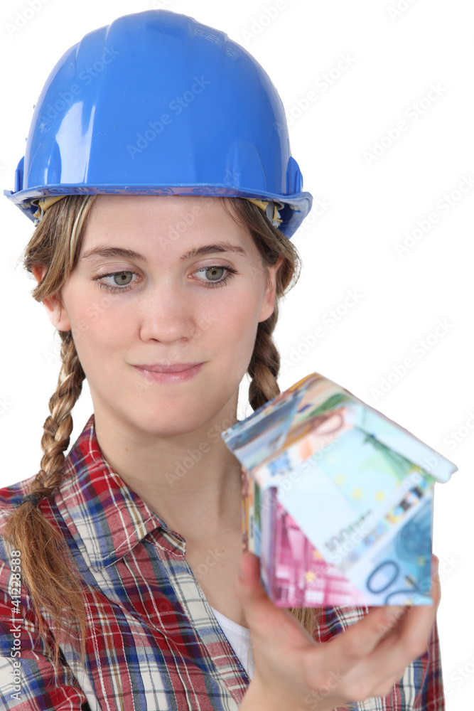 Female builder holding house made from bank notes Female builder holding house made from bank notes