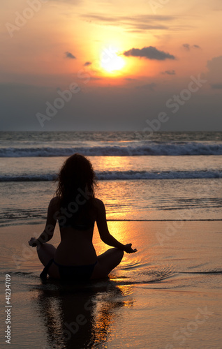 Silhouette of a beatiful woman meditating on a rock by the sea © Shchipkova Elena