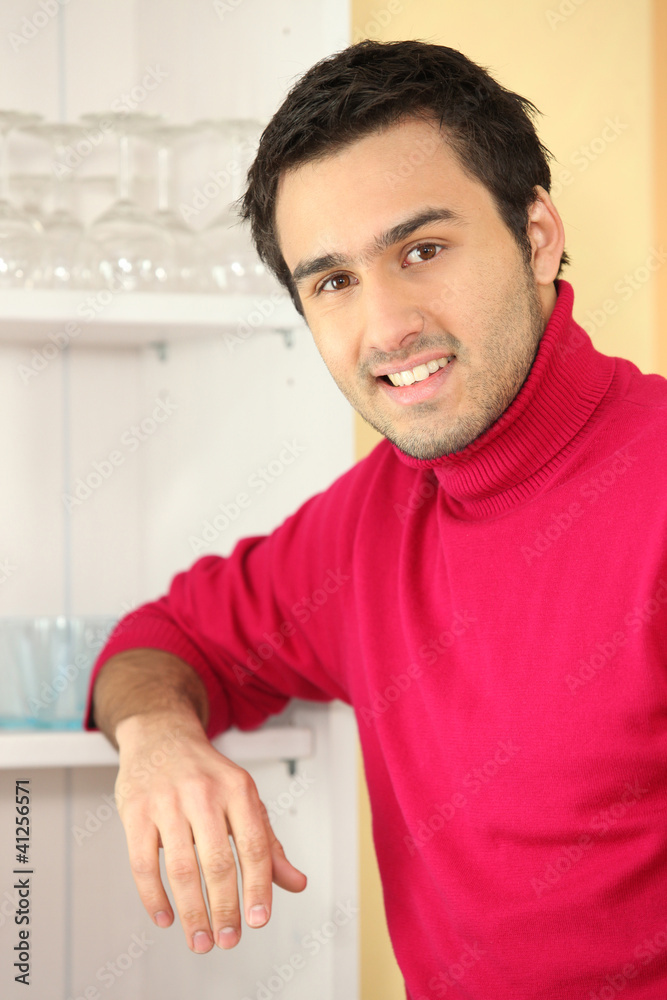 Young man standing next to a cupboard full of glasses Young man standing next to a cupboard full of glasses