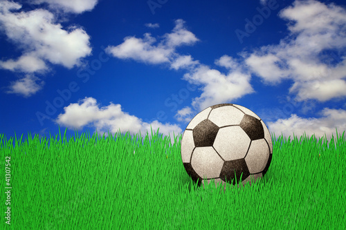 Soccer ball on grass with sky and clouds on background.