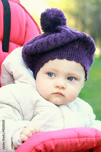 Funny baby girl in hat outdoor sit in stroller and looking. Clos