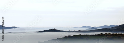 Romagna (Italy) Hills through the foggy with a little castle tower in siholuette at twilight, the fog and the clouds make up a soft white mantle. photo