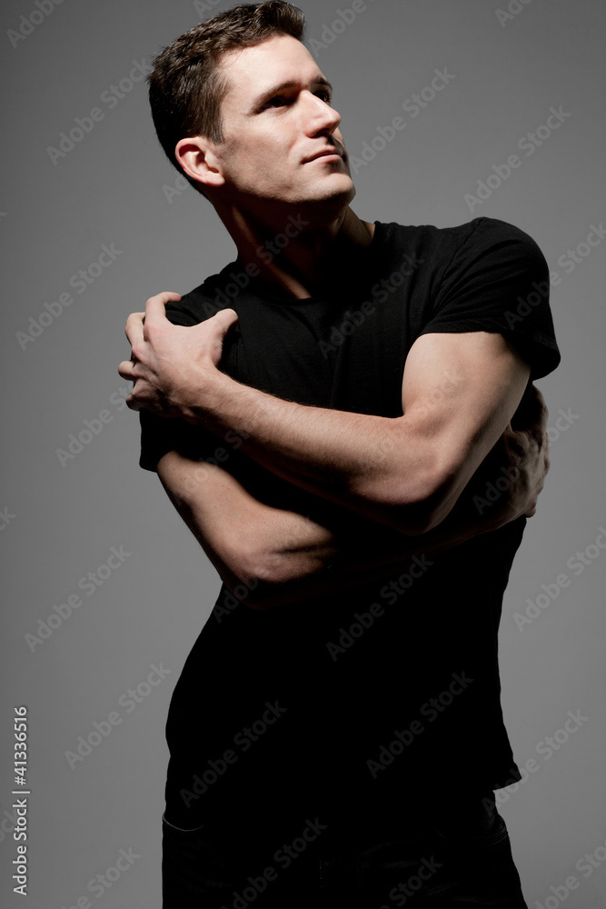 Young  man in black t-shirt posing on gray background.