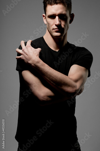 Young man in black t-shirt posing on gray background.