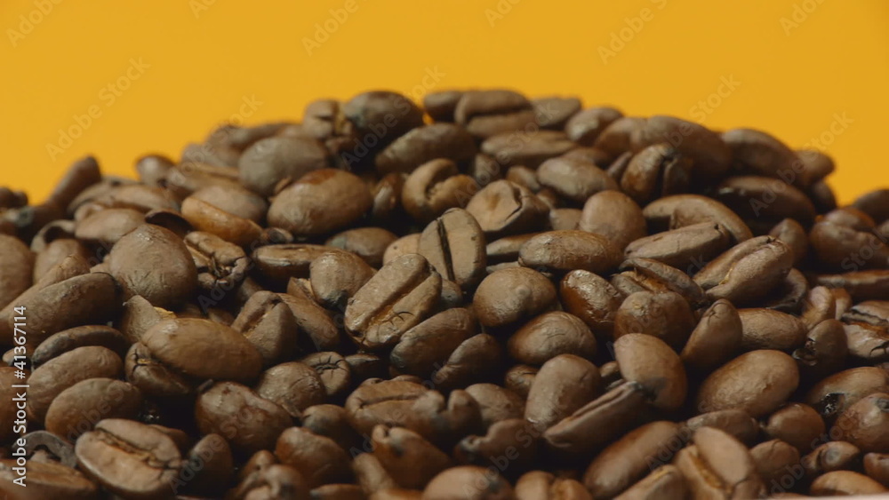 A pile of roasted coffee beans rotating on orange background A pile of roasted coffee beans rotating on orange background