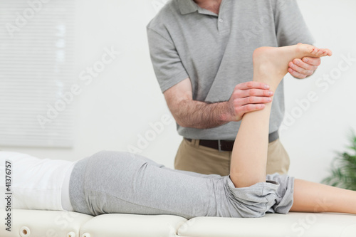 Woman lying forward while a physiotherapist examining her leg