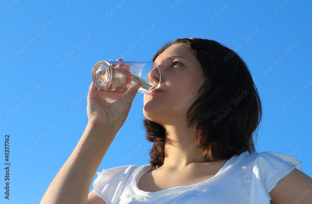 Young woman drinking water on sky background Young woman drinking water on sky background