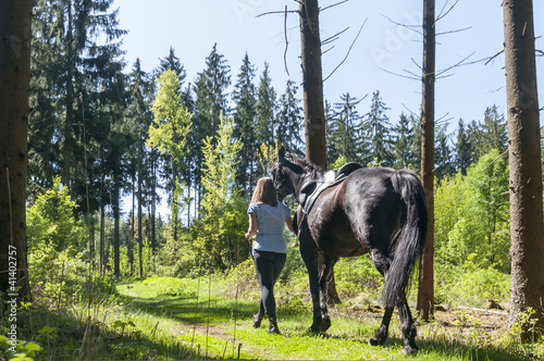 Reiterin führt Pferd im Wald