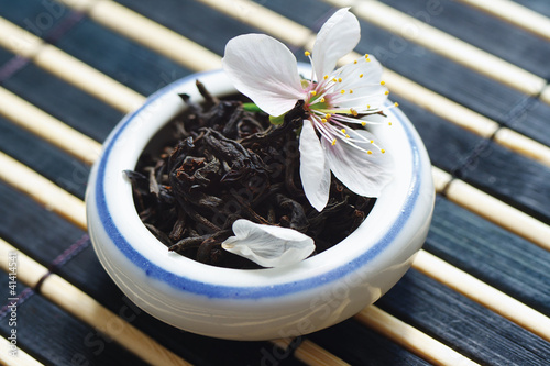 Jar of tea leaves and cherry blossoms on bamboo table cloth photo