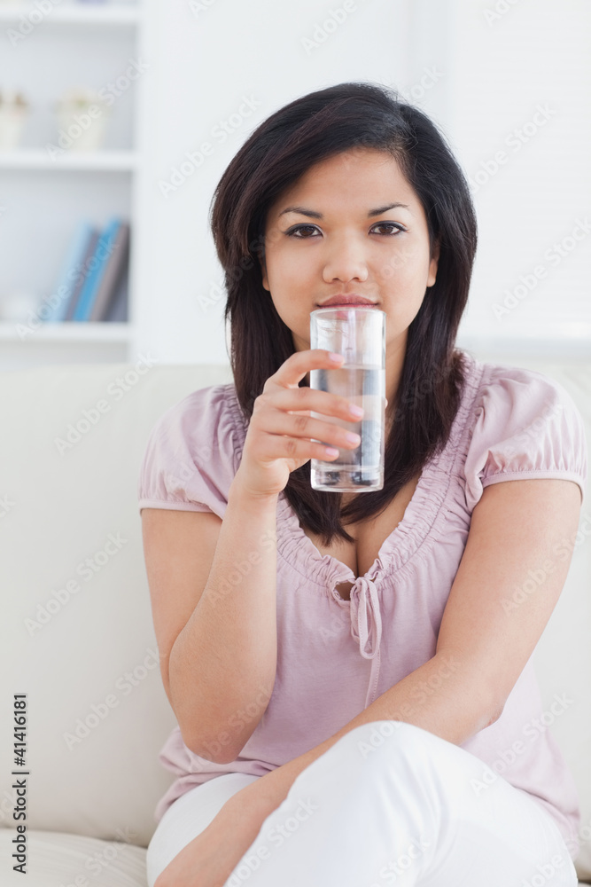Woman sitting on a couch and holding a glass of water Woman sitting on a couch and holding a glass of water