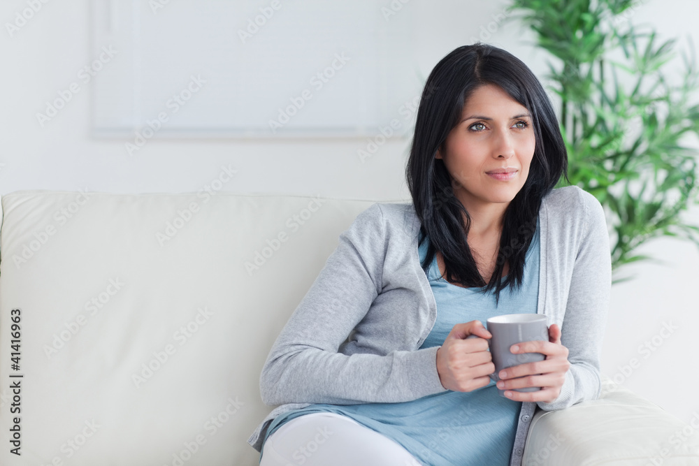 Thinking woman sits on a couch while holding a mug Thinking woman sits on a couch while holding a mug