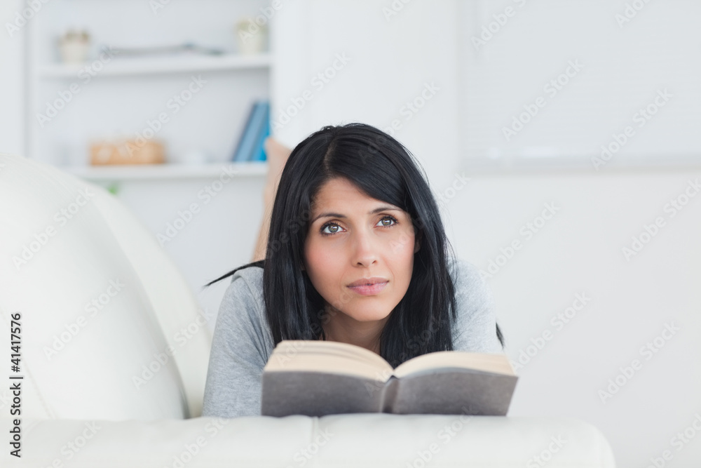 Woman holding a book while laying on a sofa Woman holding a book while laying on a sofa