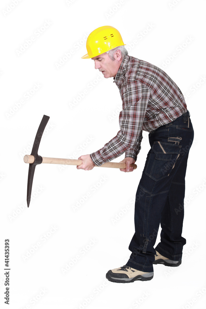 A mature construction worker using a pickaxe. A mature construction worker using a pickaxe.