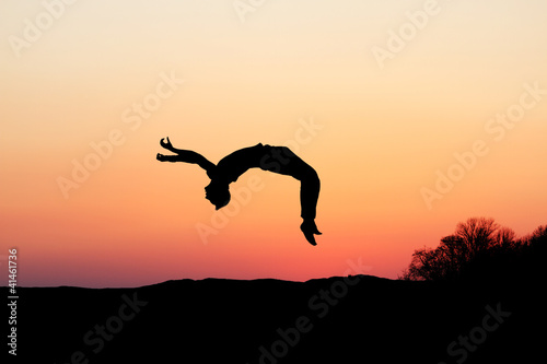 silhouette of gymnast doing a backflip in sunset photo