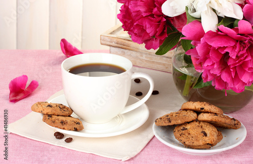cup of coffee, cookies and flowers on table in cafe