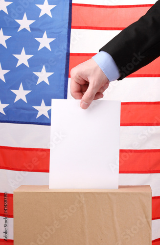 Hand with voting ballot and box on Flag of USA