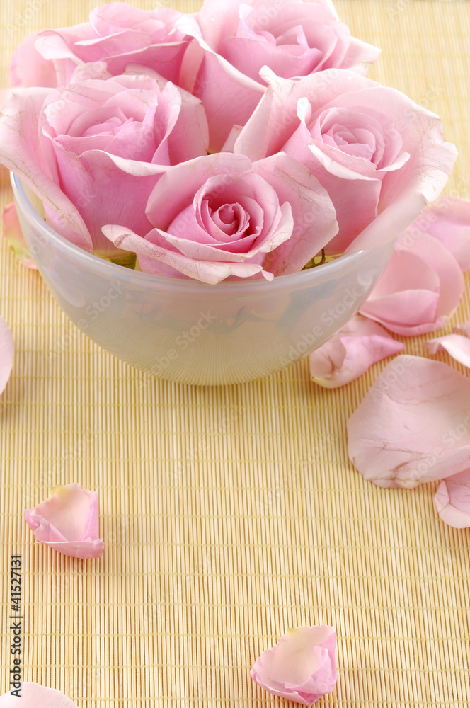 Pink rose flowers floating in a bowl with water and petal