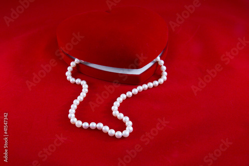 Cofanetto cuore rosso e collana di perle su fondo rosso