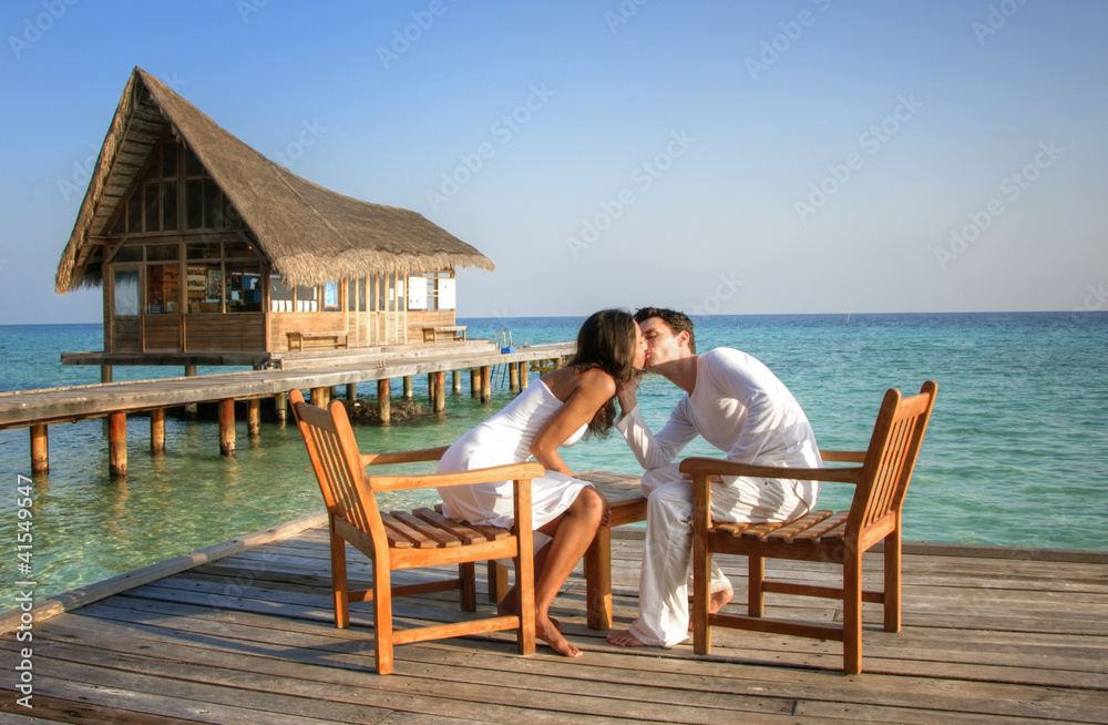 Happy love couple sitting on a jetty at the beach (maldives)