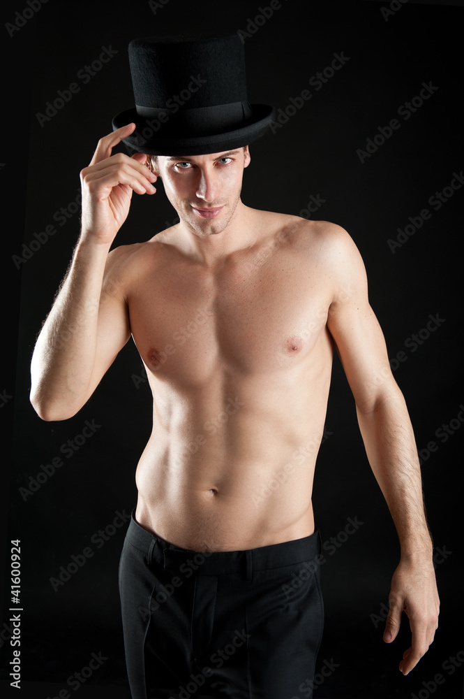 Young magician shirtless with cylinder against black background. Young magician shirtless with cylinder against black background.