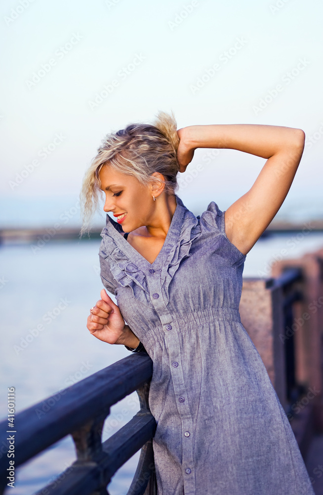 blond woman in grey dress on a quay.