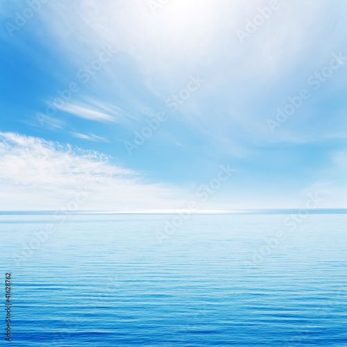 light waves on blue sea and cloudy sky with sun