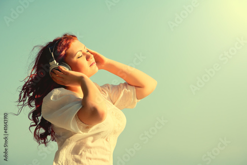 beautiful redhead girl with long hair enjoys music with headphon photo