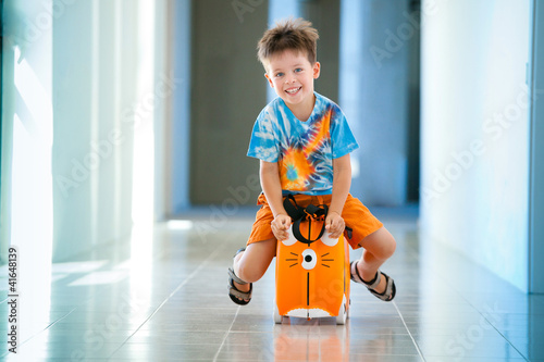 Boy laughs and sitting on a suitcase at airport