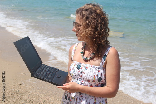 Curly hair young woman with her laptop at the beach