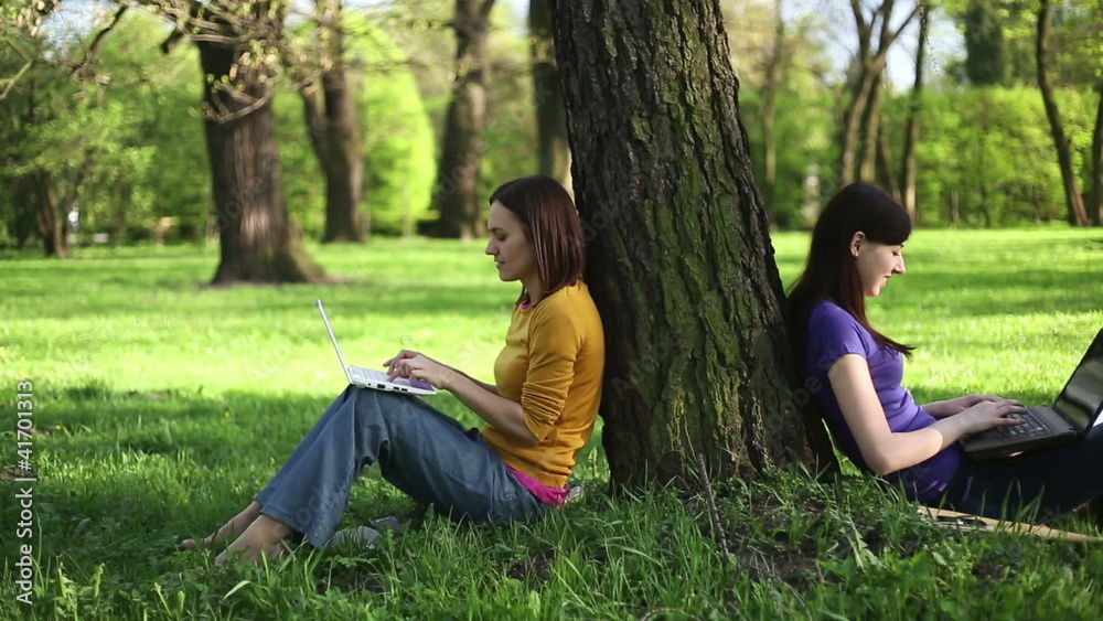 Two girls sitting in the park with laptops, tracking shot Two girls sitting in the park with laptops, tracking shot