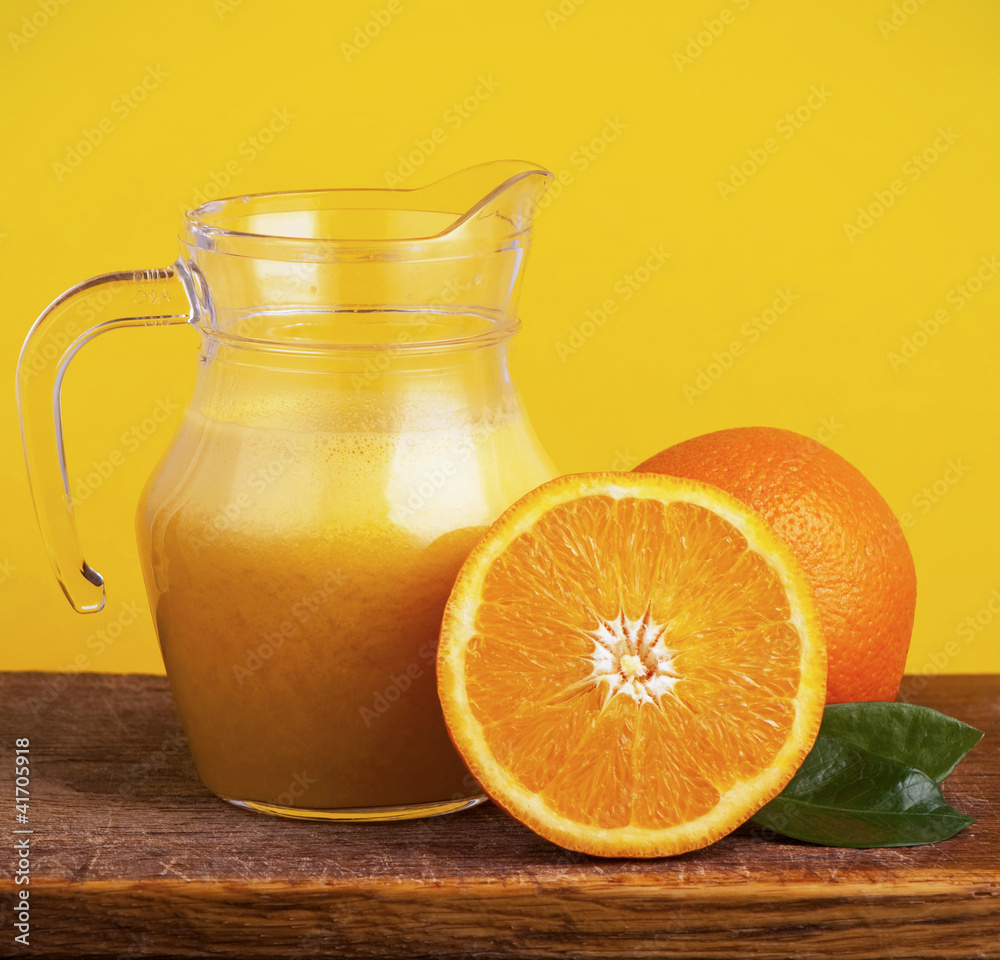 Orange juice in pitcher and oranges. Isolated on yellow Orange juice in pitcher and oranges. Isolated on yellow