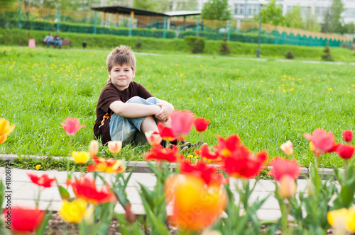 The boy sitting next to the flowerbed with tulips