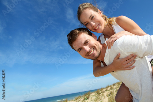 Bild auf Leinwand Man giving piggyback ride to girlfriend on a sand dune