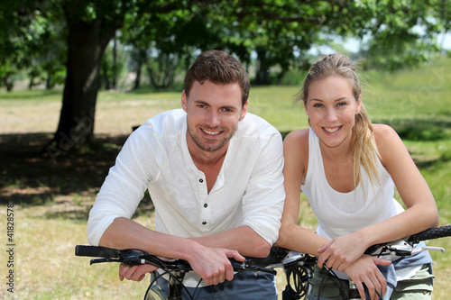 Portrait of cheerful couple riding bicycle in countryside