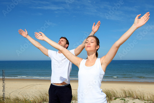 Couple meditating at the beach with arms up