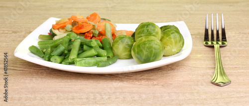 Mixed vegetables on plate on wooden table on green background