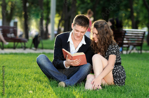 Boy and girl reading a book sitting on the grass © Аrtranq