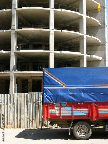 Roter Lastwagen mit Pritsche und blauer Plane vor dem Rohbau eines Hochhaus auf einer Baustelle im Sonnenschein in Erenköy in Sahrayicedit in Istanbul am Bosporus in der Türkei photo