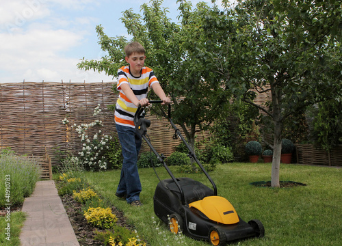 Teen boy mows the lawn mower electric