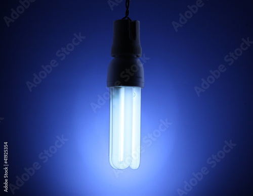 A lit energy saving light bulb on blue background © Africa Studio