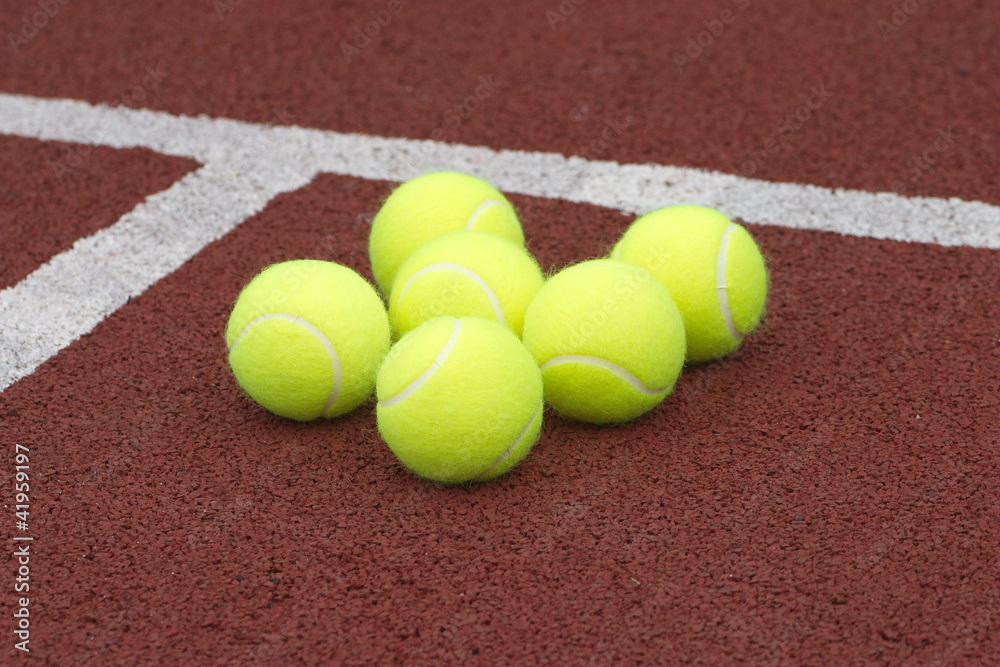Yellow tennis balls lays on brown court closeup