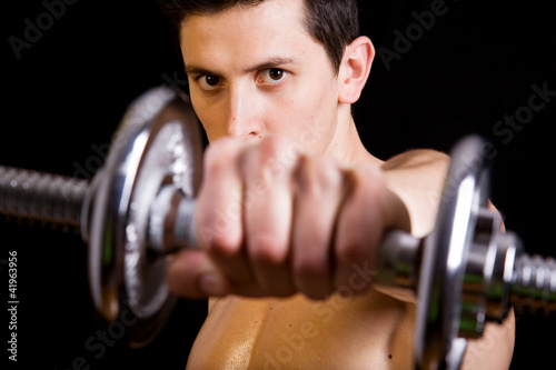 Young muscular man lifting weights on black background