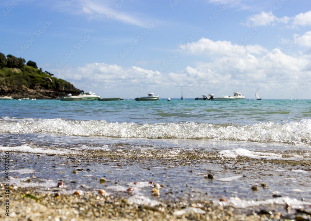Pebble beach with a running wave against mountain, boats and blu Pebble beach with a running wave against mountain, boats and blu