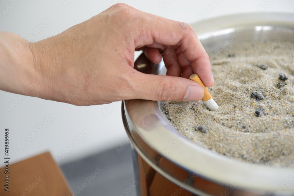 Male hand Stubbing Out Cigarette in sand ashtray bin