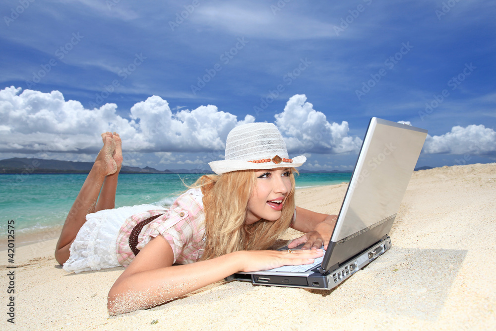 砂浜に寝転びインターネットを楽しむ女性