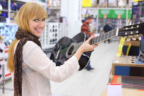 Happy girl wearing scarf holds guitar in supermarket